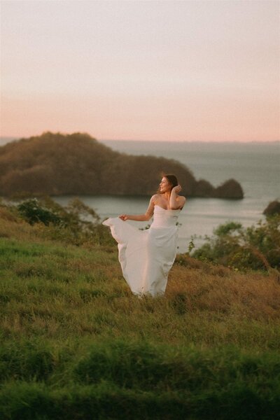 A bride on a grassy clifftop above the ocean at sunset